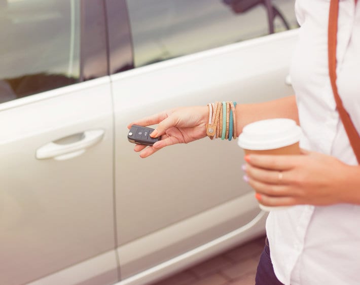 Woman opening car with keys while holding coffee