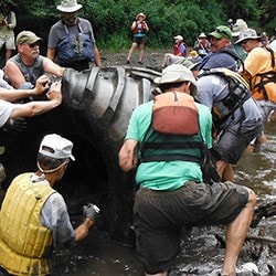 rolling a giant tire across a stream for the Spent Tire Initiative